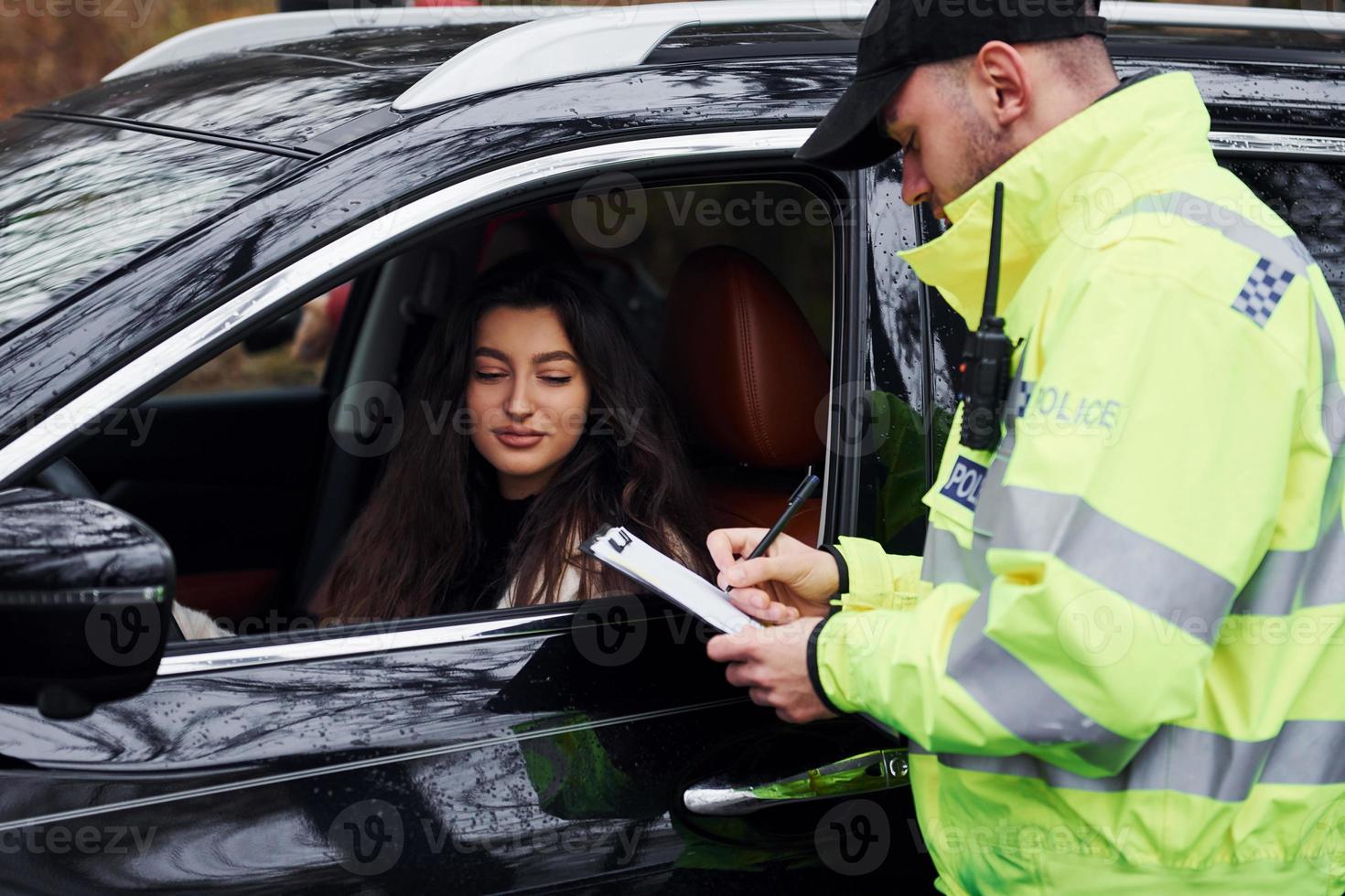 Male police officer in green uniform with notepad checking vehicle on the road photo