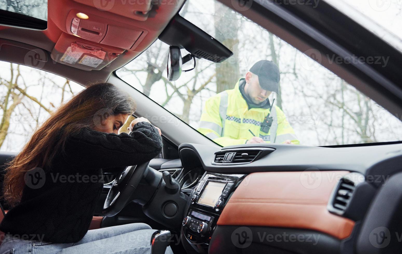 chicas se siente mal. oficial de policía masculino con uniforme verde revisando el vehículo en la carretera foto