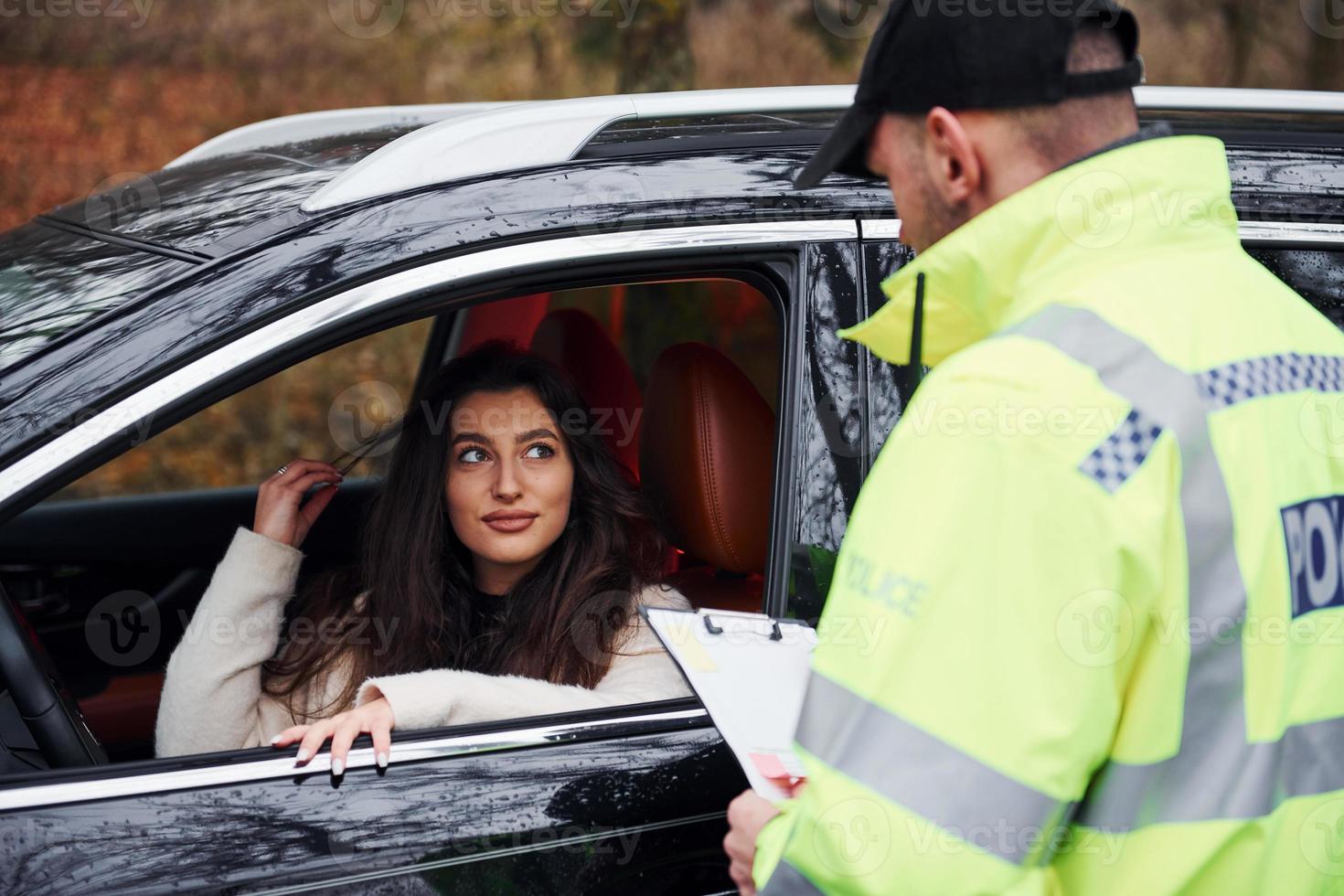 Male police officer in green uniform with notepad checking vehicle on the road photo