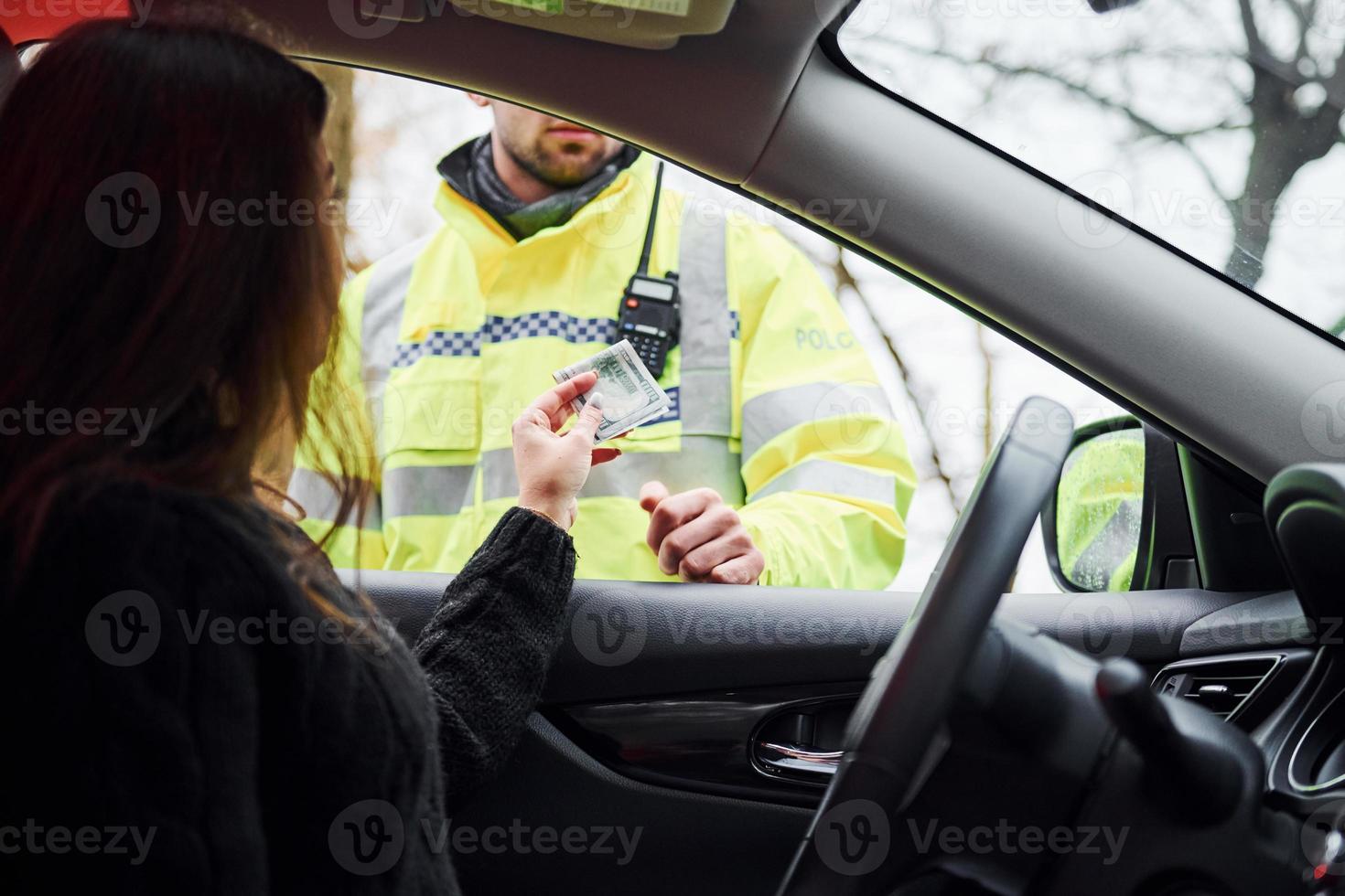 Male police officer in green uniform checking vehicle on the road. Woman trying to give bribe photo