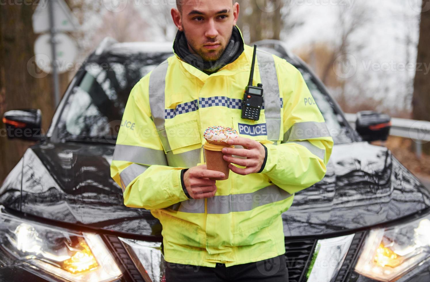 Male police officer in green uniform taking a break with donut on the road photo