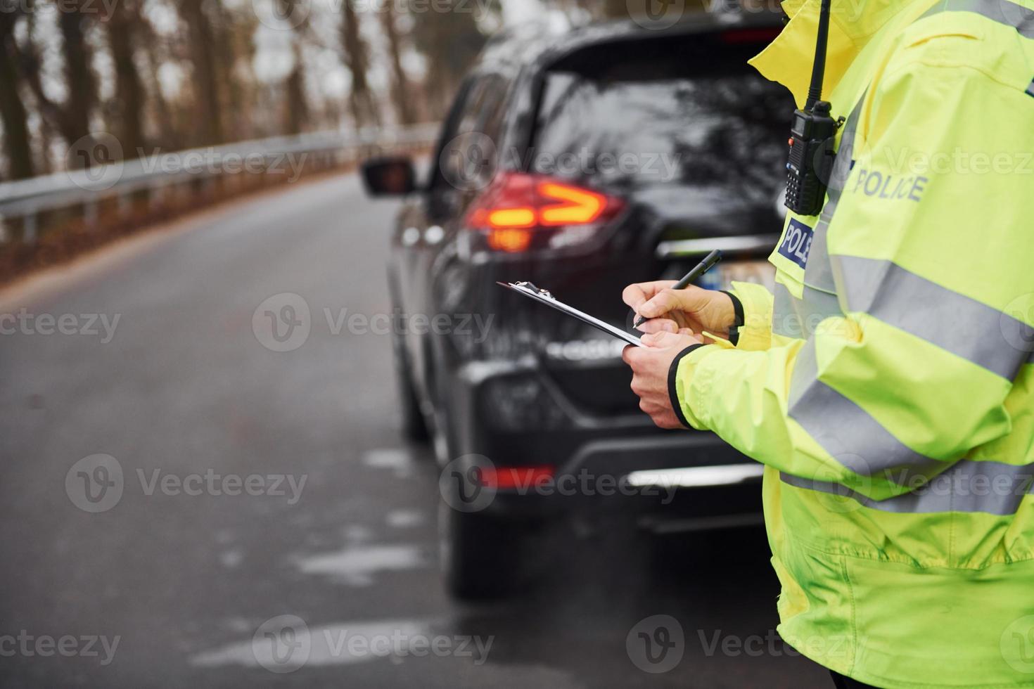 Male police officer in green uniform standing with notepad near car photo