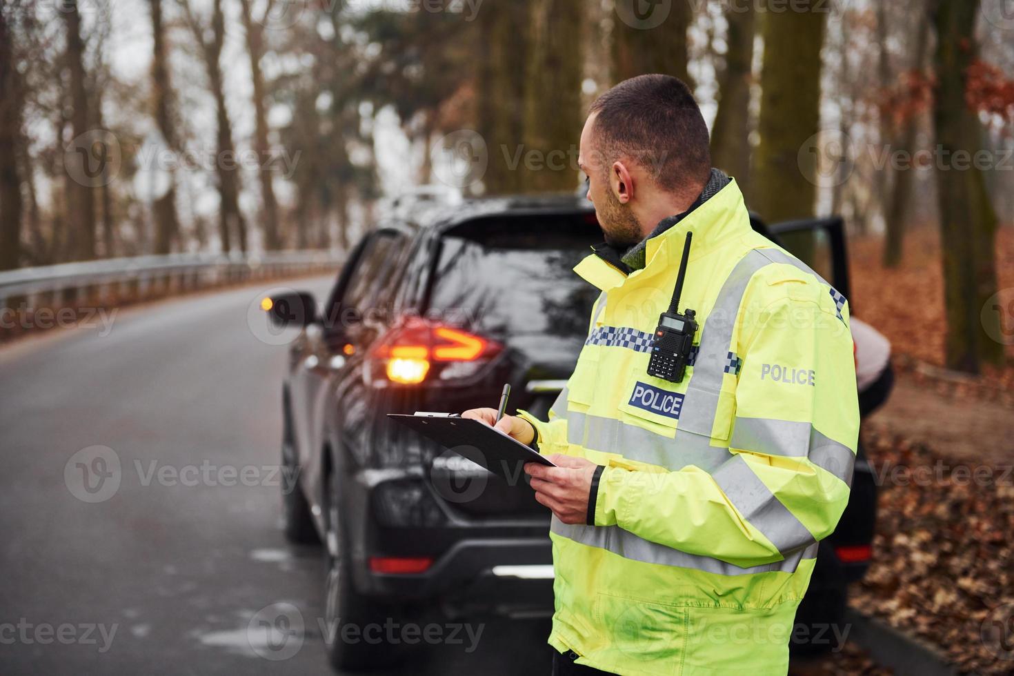 Male police officer in green uniform standing with notepad near car photo