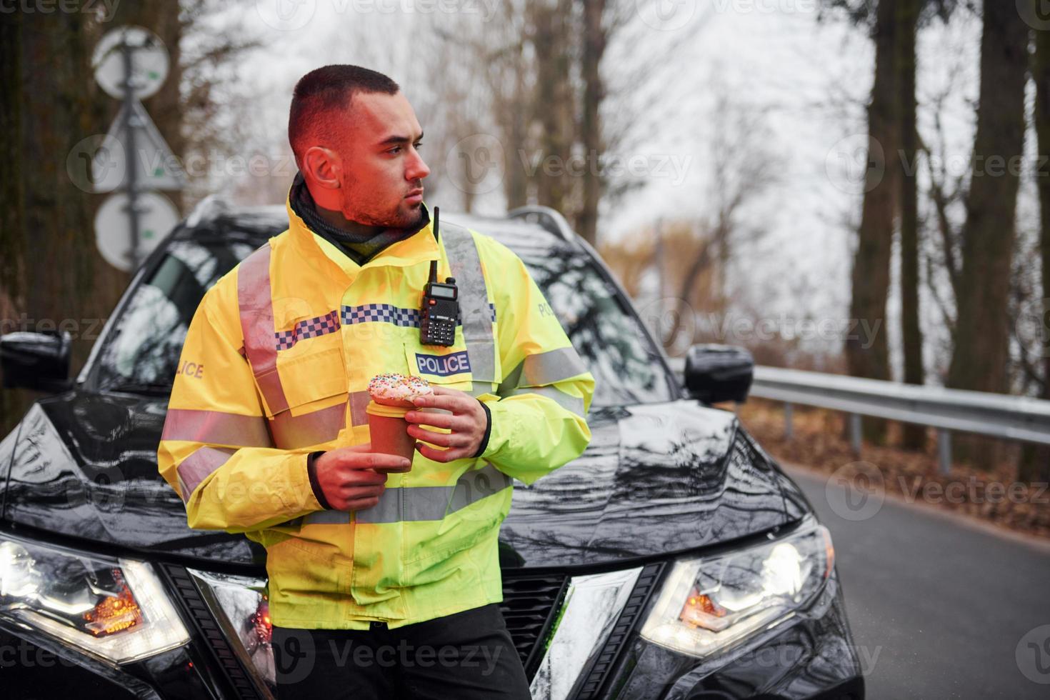 Male police officer in green uniform taking a break with donut on the road photo