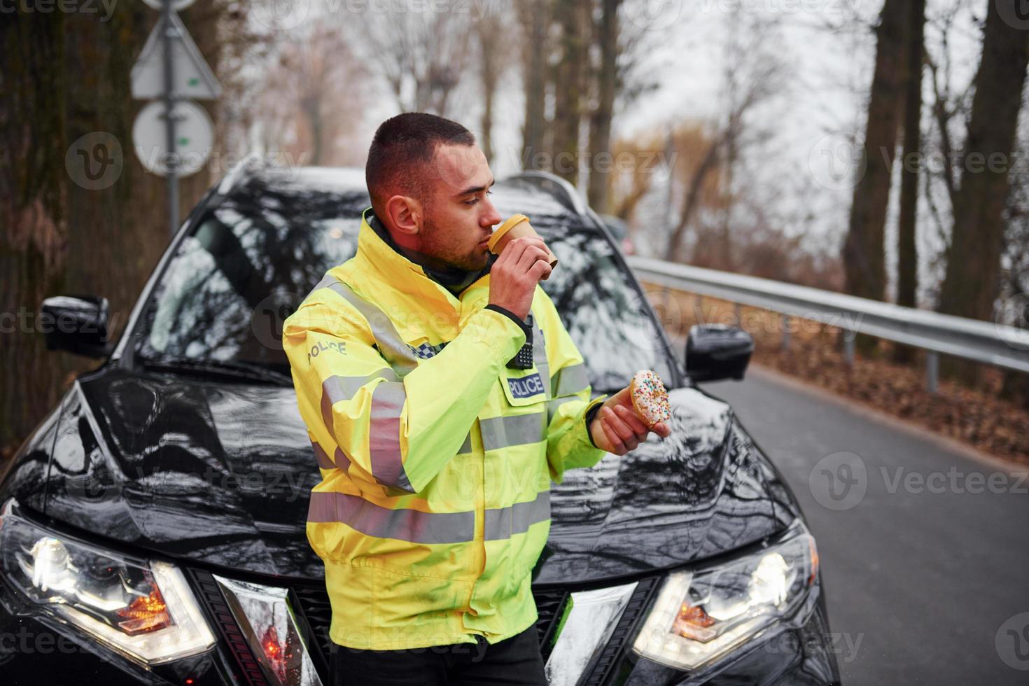 oficial de policía masculino con uniforme verde tomando un descanso con donut en la carretera foto