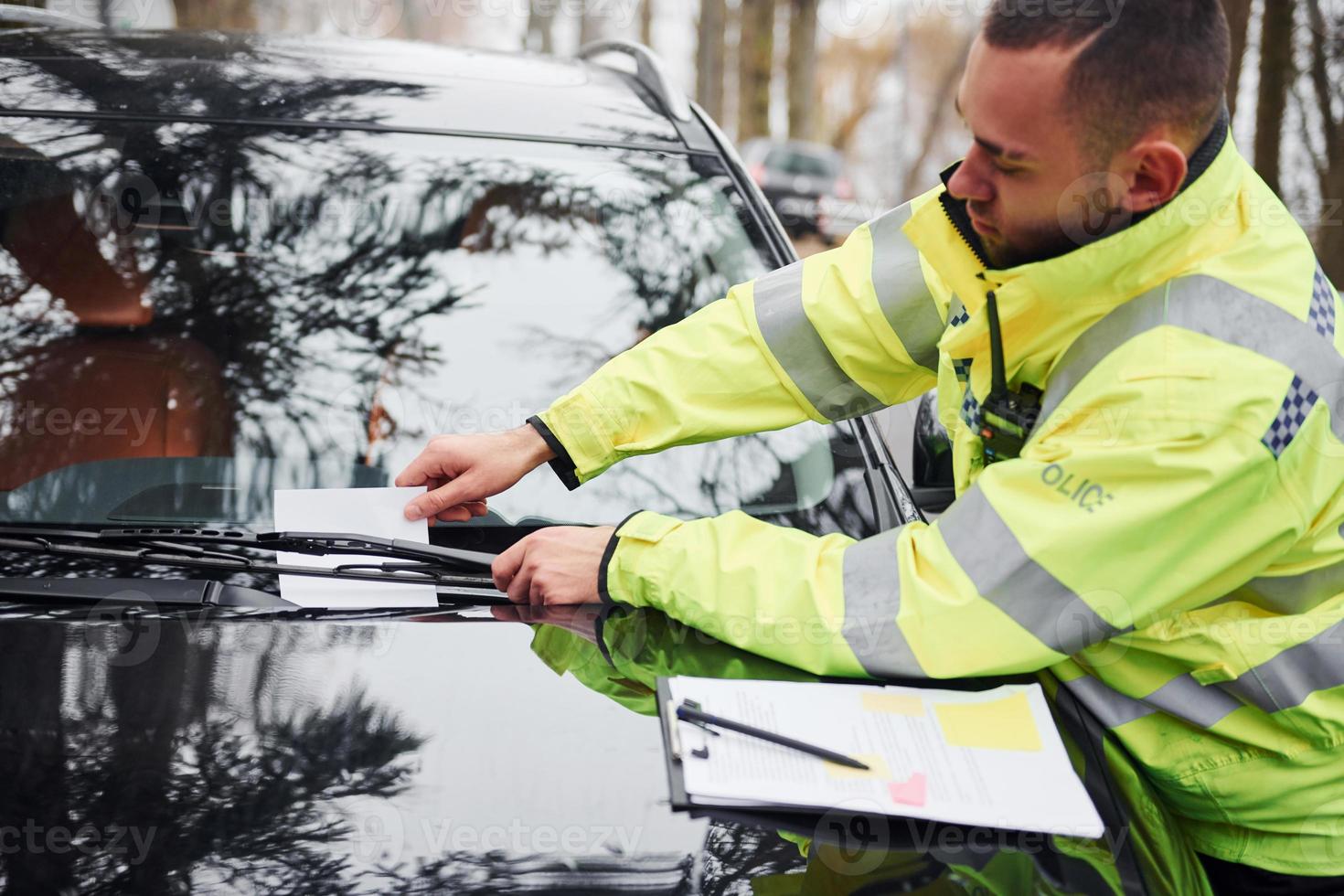 Male police officer in green uniform putting fine list to the vehicle photo