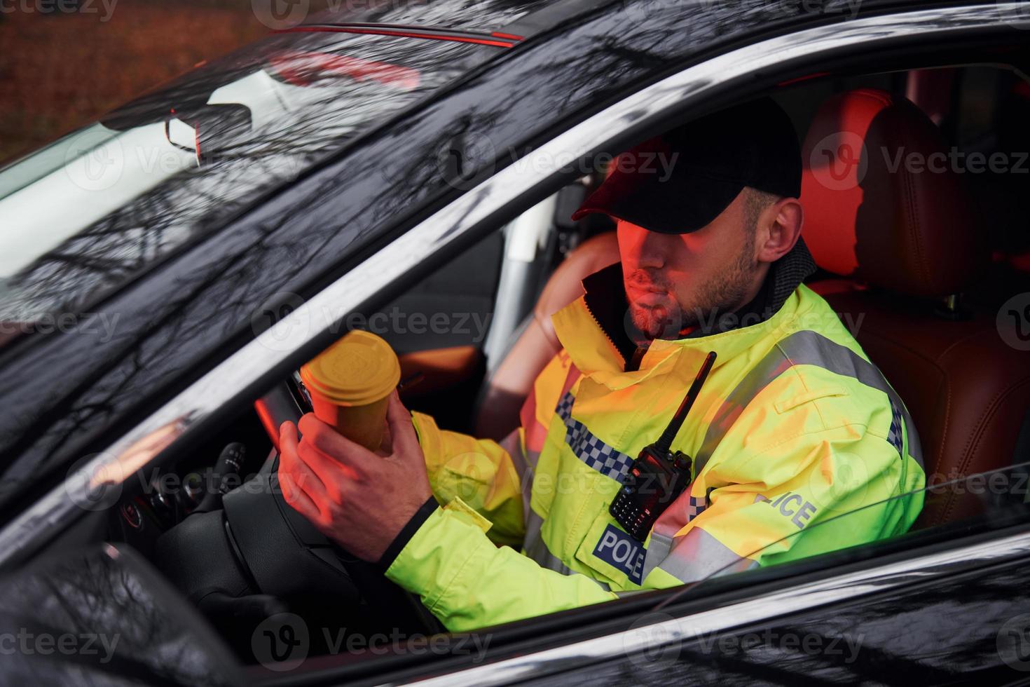 Male police officer in green uniform sitting in automobile with cup of drink photo