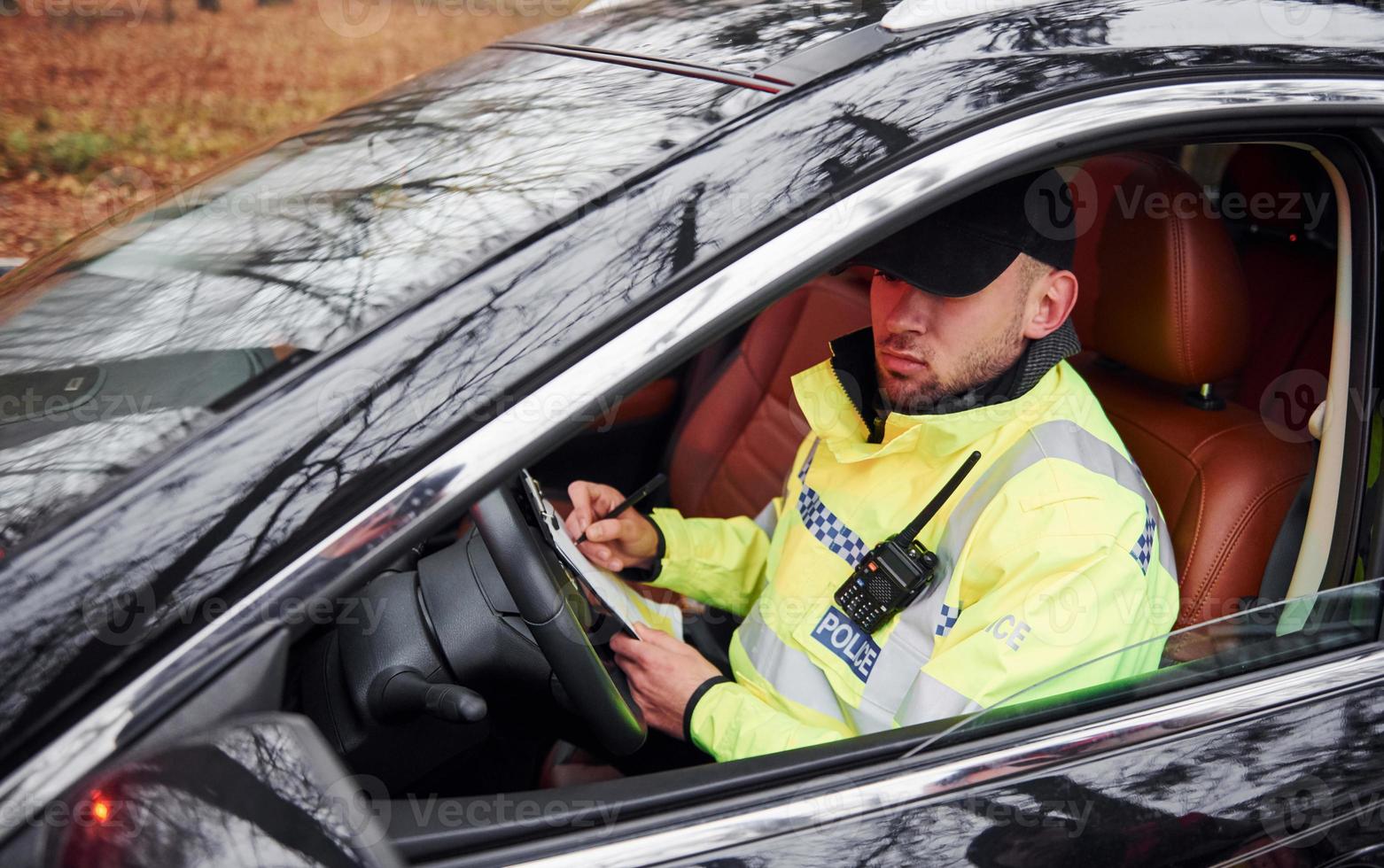 Male police officer in green uniform sitting in automobile and working with documents photo