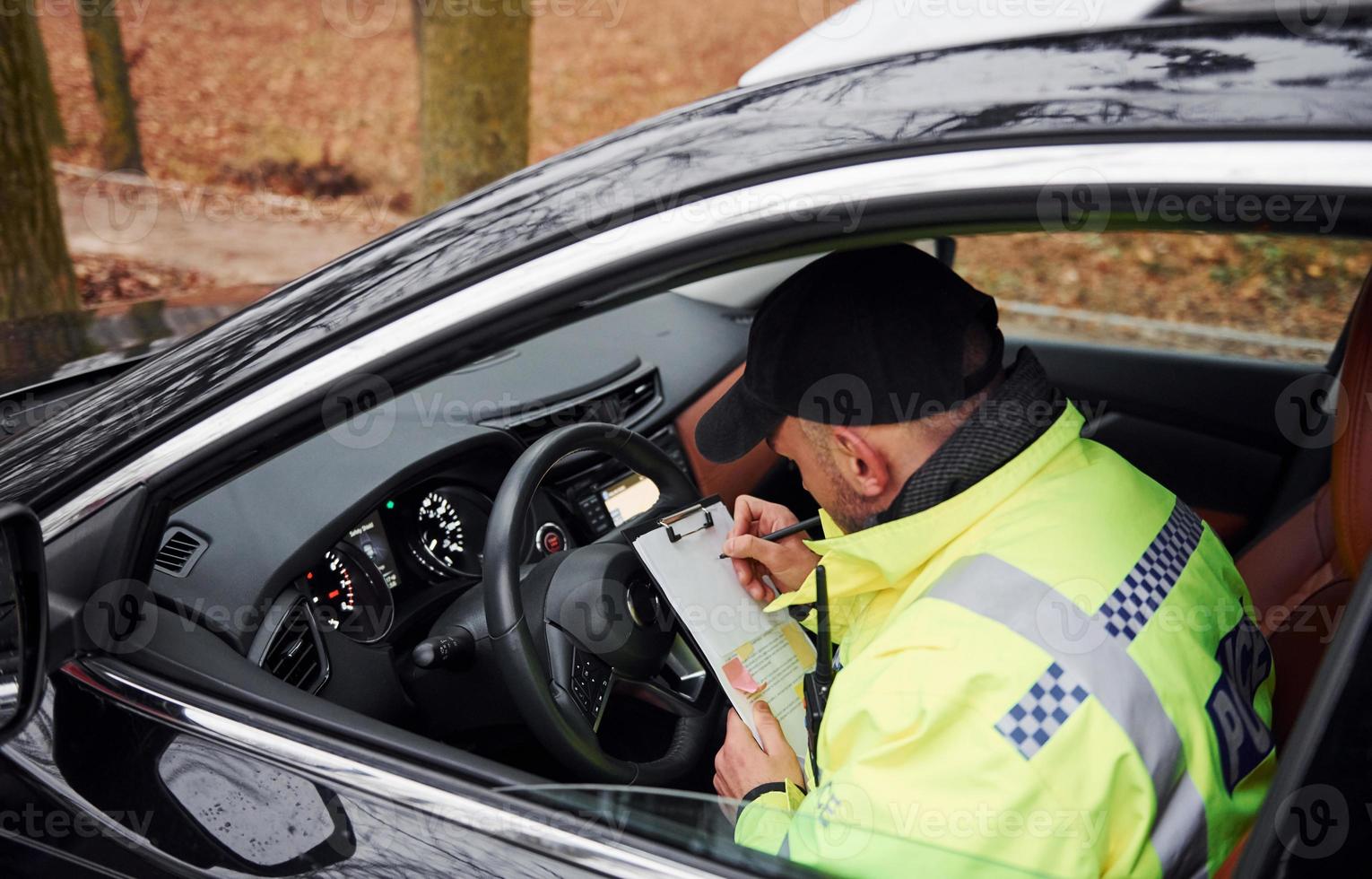 Male police officer in green uniform sitting in automobile and working with documents photo