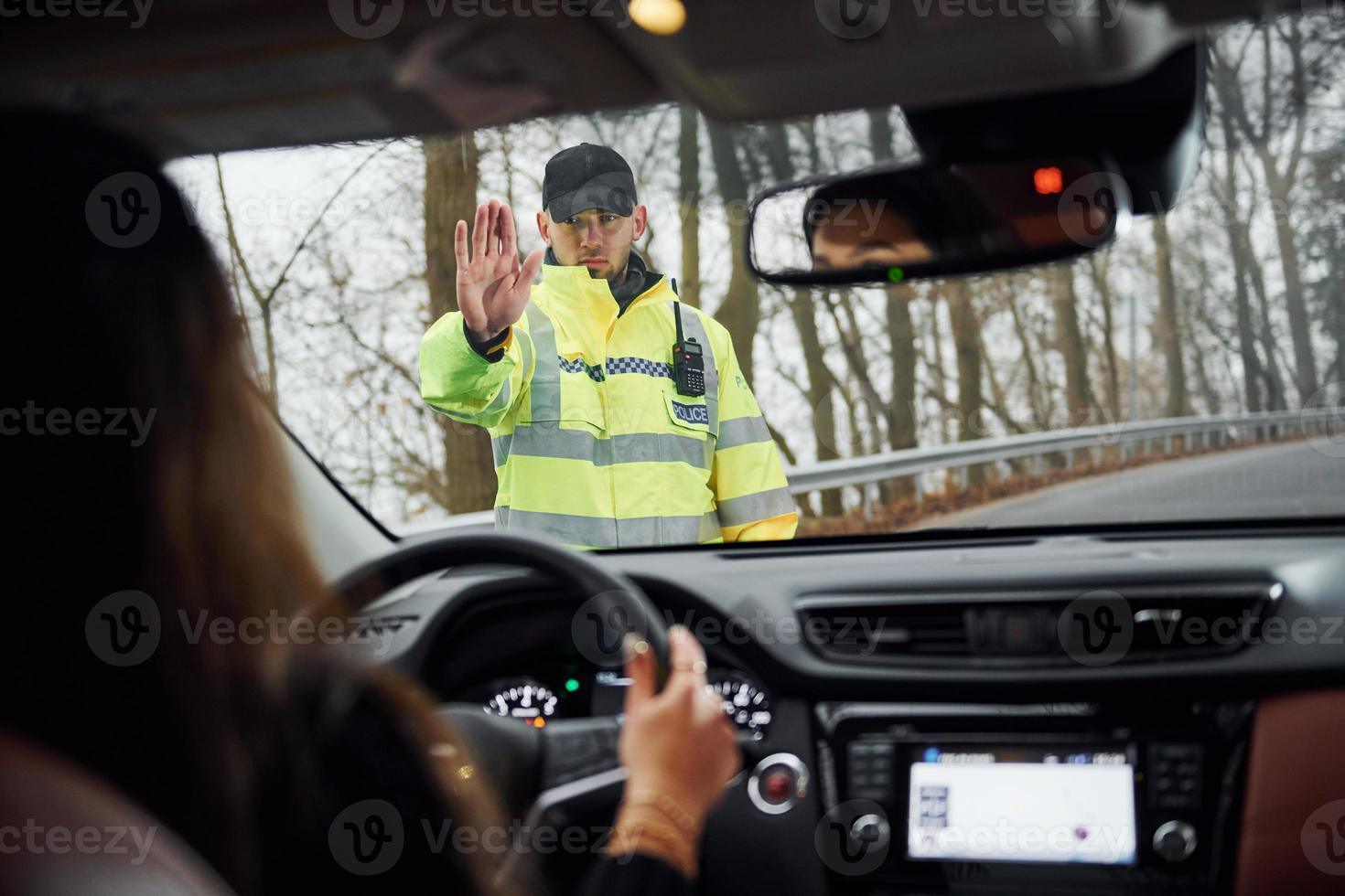 Male police officer in green uniform stops vehicle with female driver on the road photo