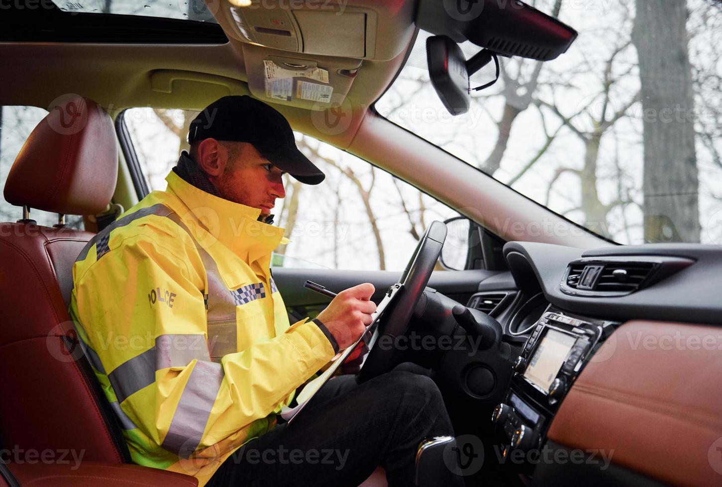 Male police officer in green uniform sitting in automobile and working with documents photo