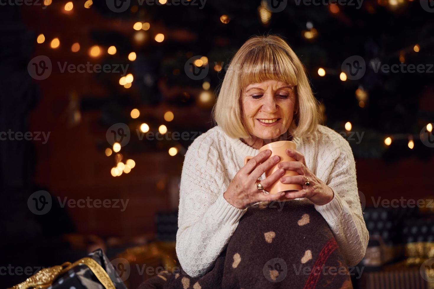 Portrait of grandmother that standing in New year decorated room with cup of drink photo