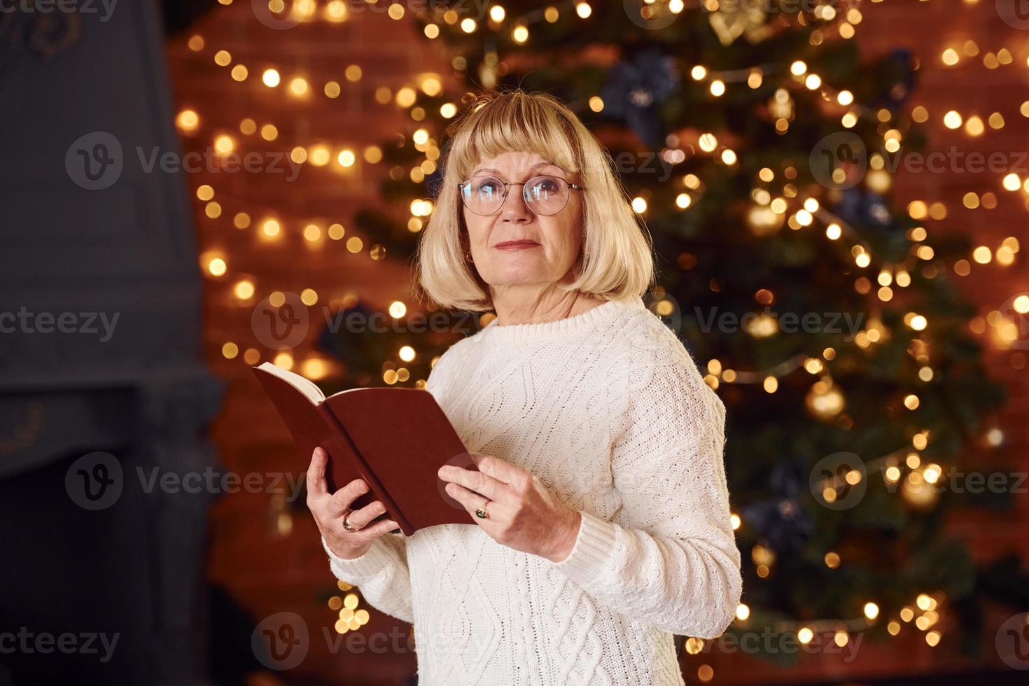 Portrait of grandmother that standing in New year decorated room with book photo