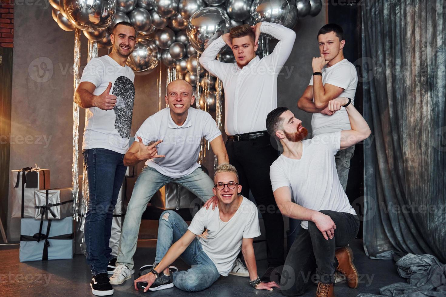 grupo de hombres alegres parados juntos en una habitación decorada con navidad y posando para una cámara foto