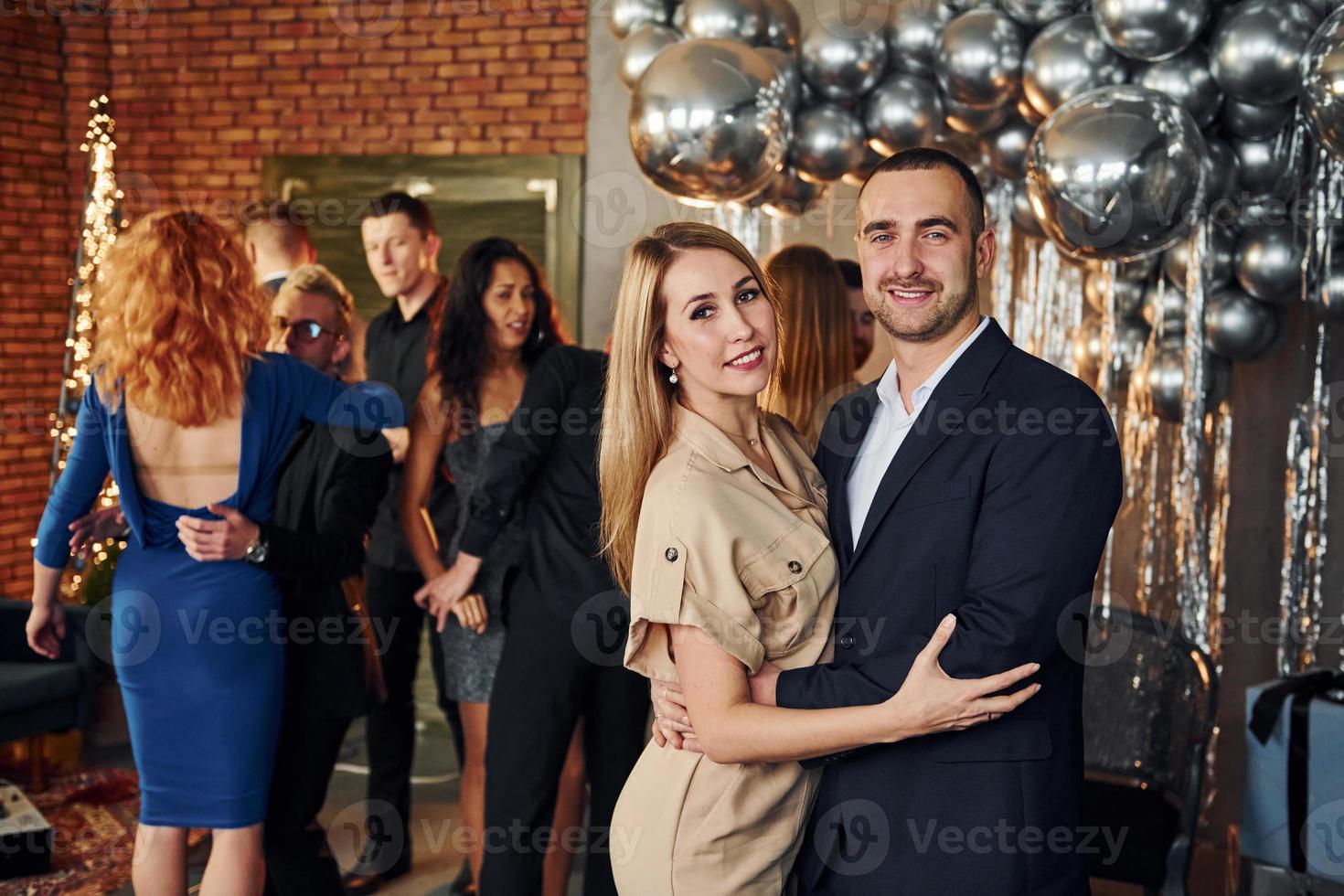 elegante pareja joven de pie junto a sus amigos en una habitación decorada con navidad y celebrando el año nuevo foto