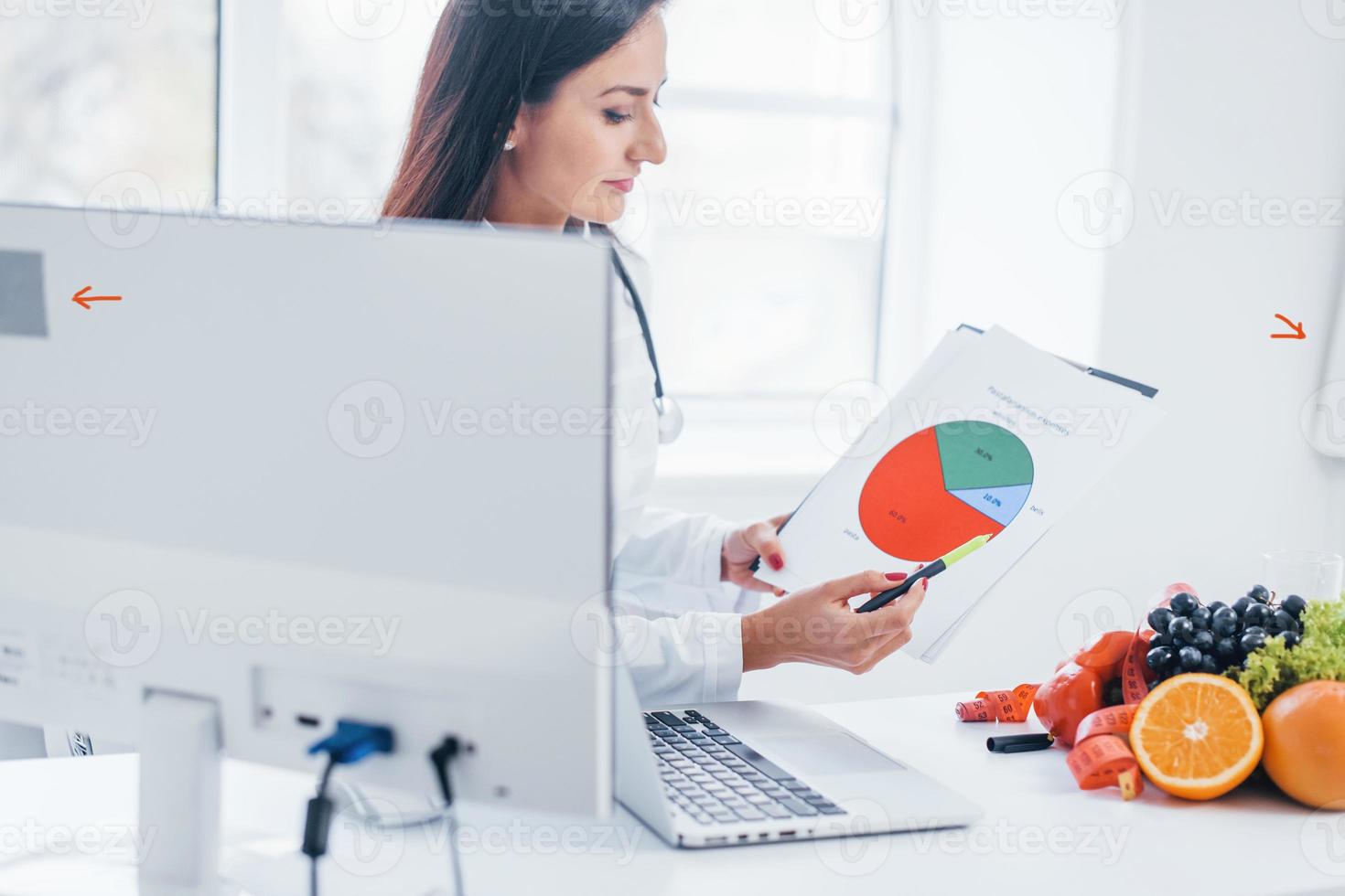 Female nutritionist in white coat sitting indoors in the office at workplace photo