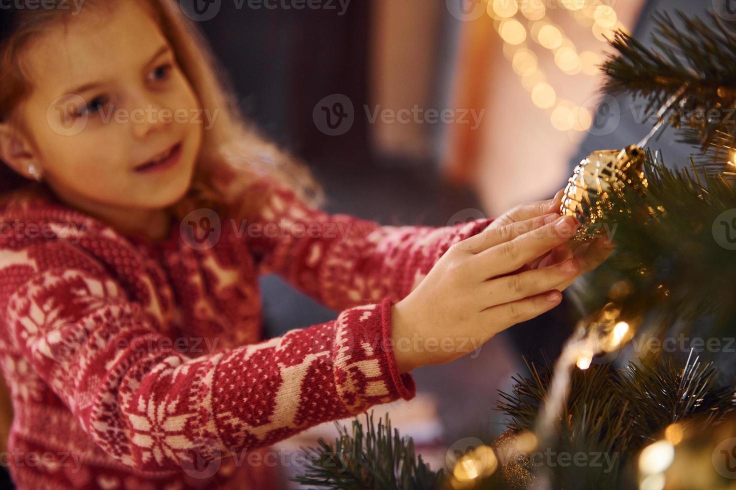 Cute little girl decorating christmas tree indoors at new year holidays photo