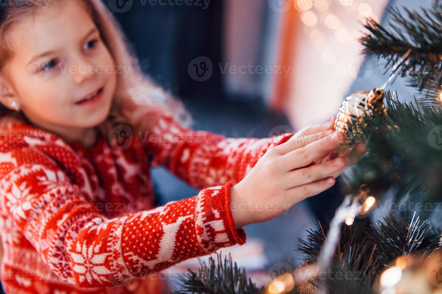 Cute little girl decorating christmas tree indoors at new year holidays photo