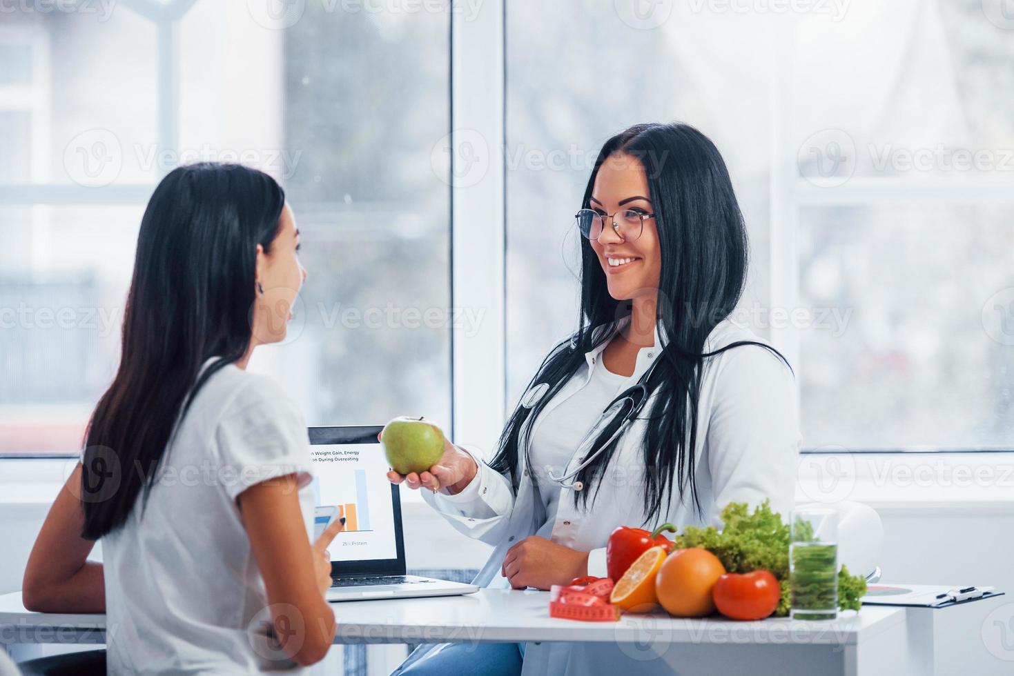 Female nutritionist with laptop gives consultation to patient indoors in the office photo