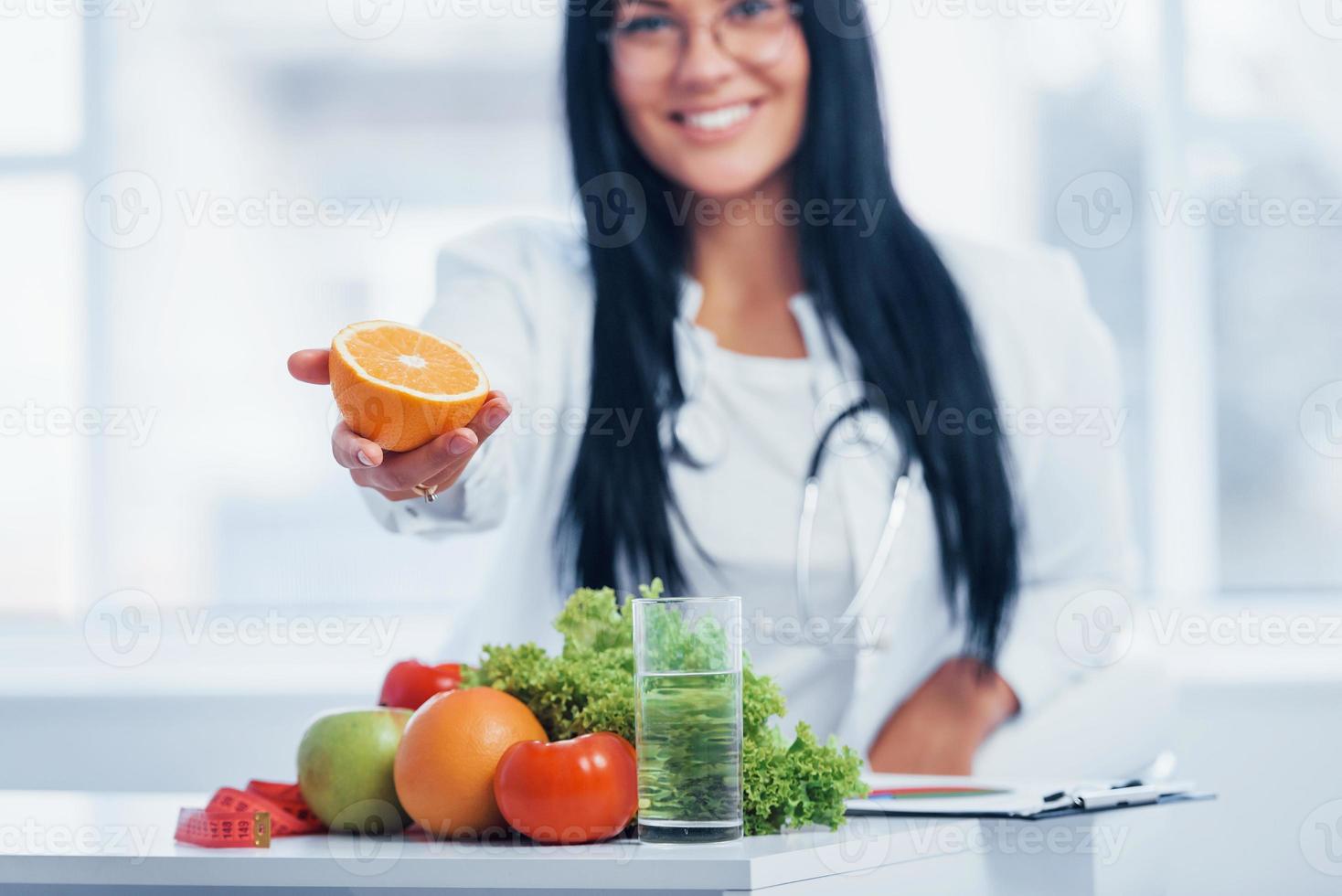 Female nutritionist in white coat holding orange in hand photo