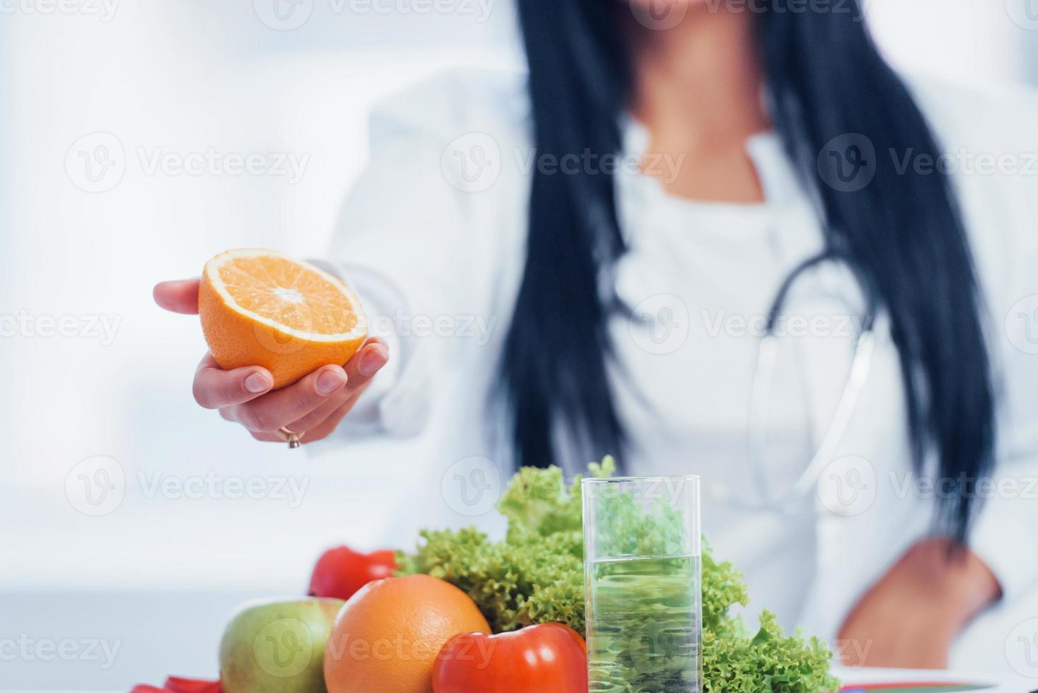 Female nutritionist in white coat holding orange in hand photo