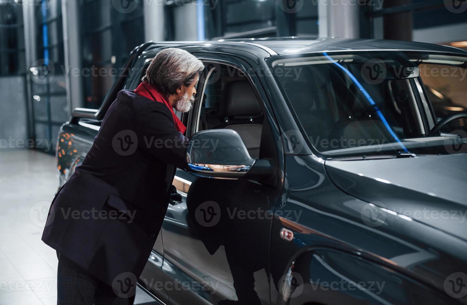 Fashionable old man with grey hair and mustache looking for a new car indoors in salon photo