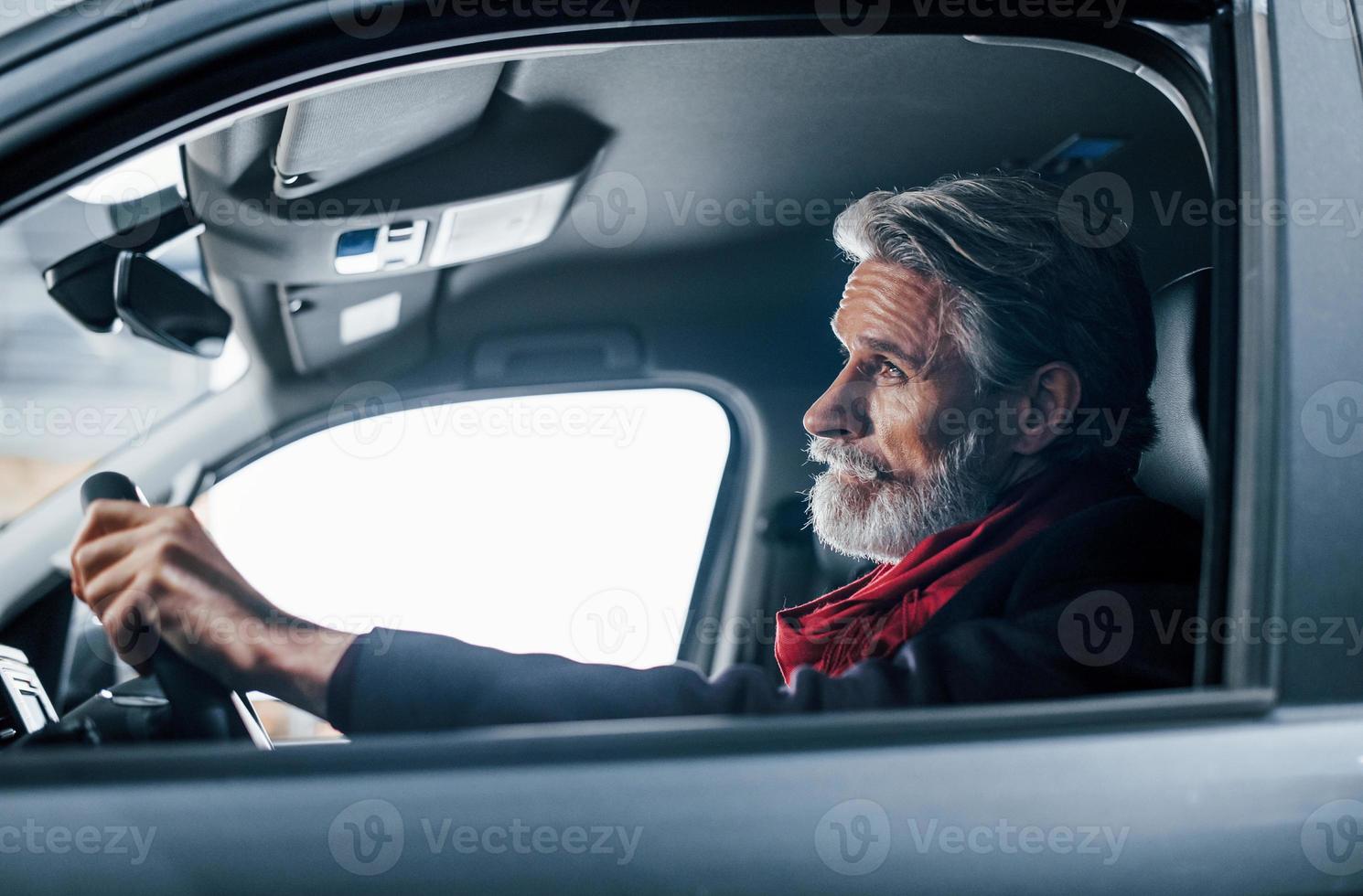 Modern stylish senior man with grey hair and mustache is in the modern car photo