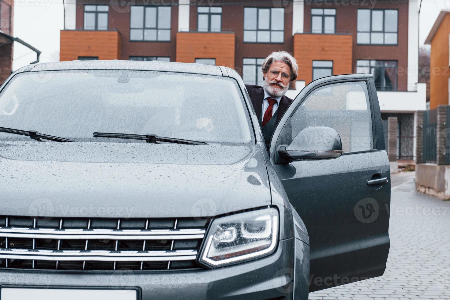 Fashionable senior man with gray hair and beard sitting in his modern new car on the street photo