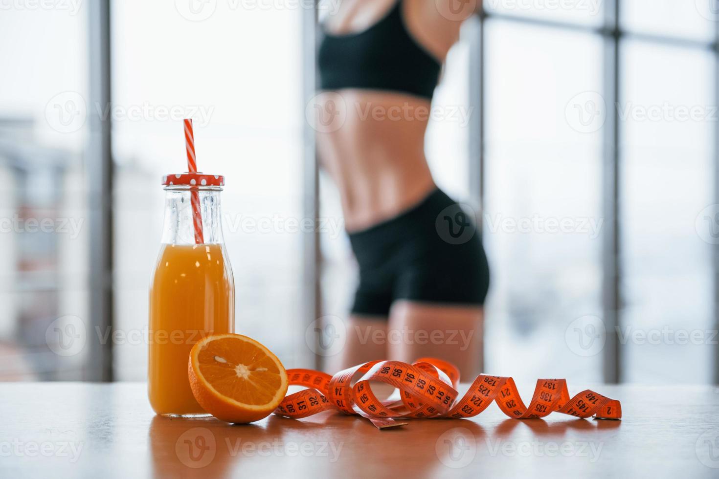 Woman with sportive body standing indoors near table with orange juice and measuring tape photo