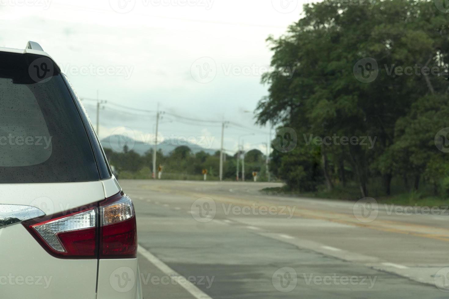 parte trasera del coche familiar blanco conduciendo por la carretera vacía. el destino es un camino curvo bordeado de árboles verdes y postes eléctricos. foto