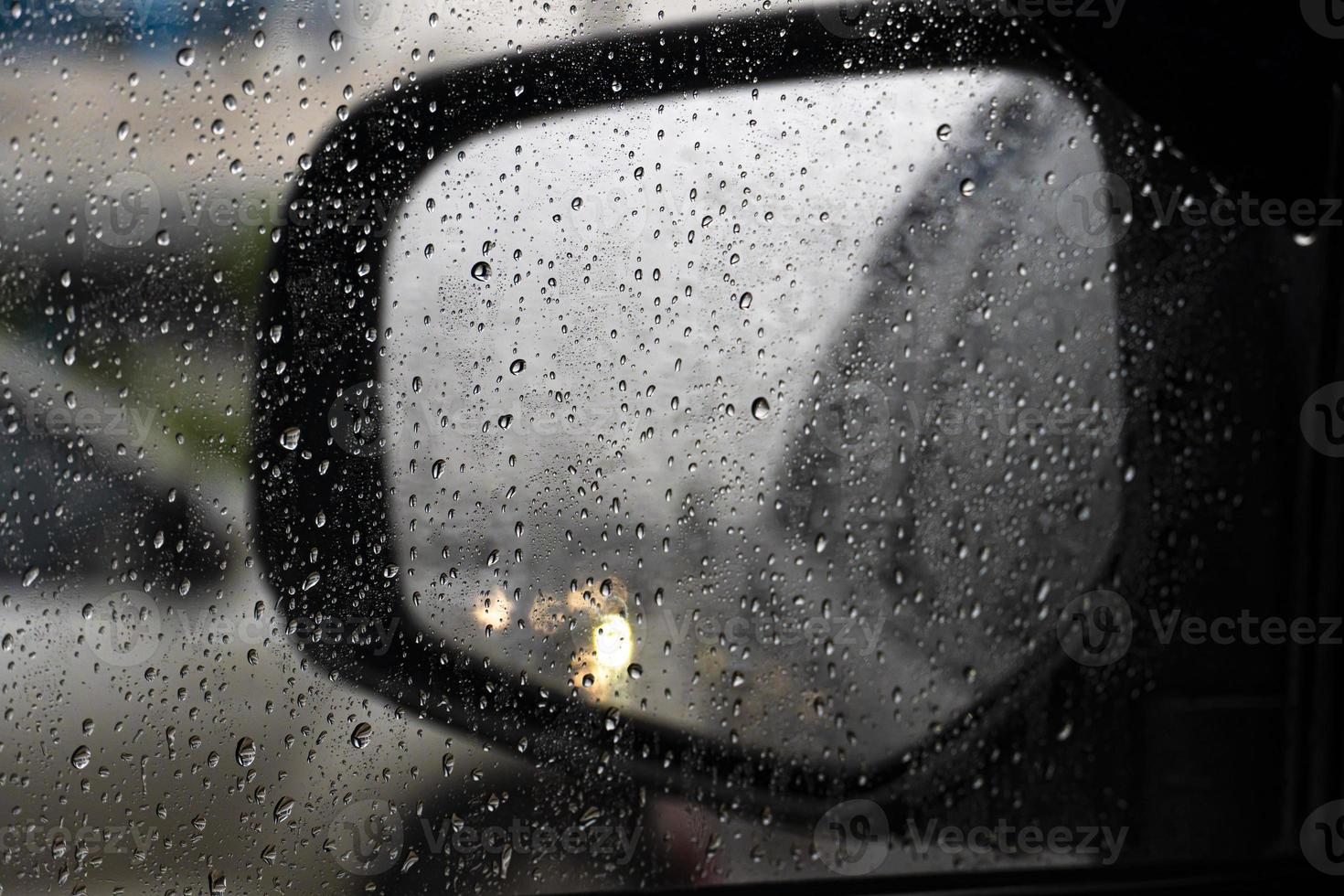 Drop of rain on the glass of car. Blurred of mirror wing with light from the car's headlights flashed twice. photo