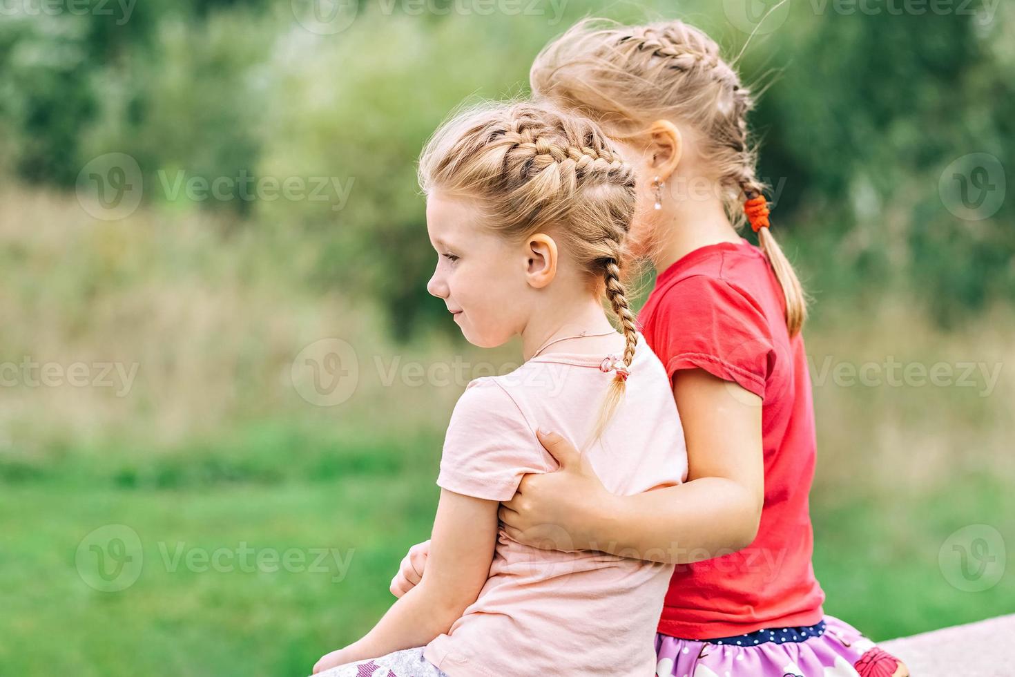 Two girls toddler sisters sit hugging on the bridge in the park. Support photo