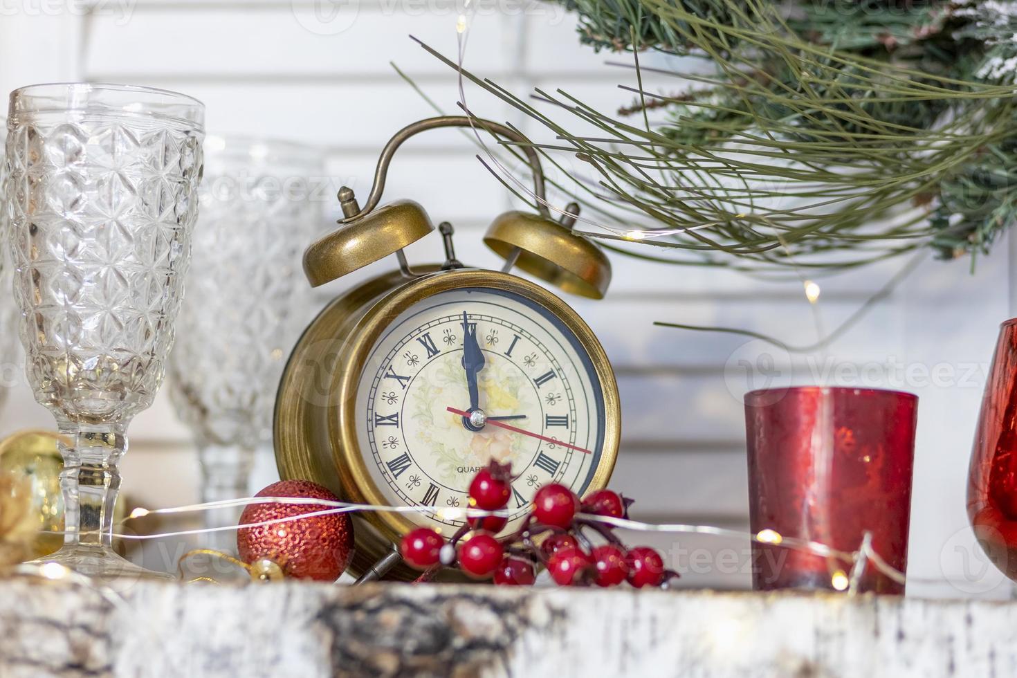 There is an alarm clock with Christmas decorations on the shelf. On the clock five minutes before the new year, Christmas photo