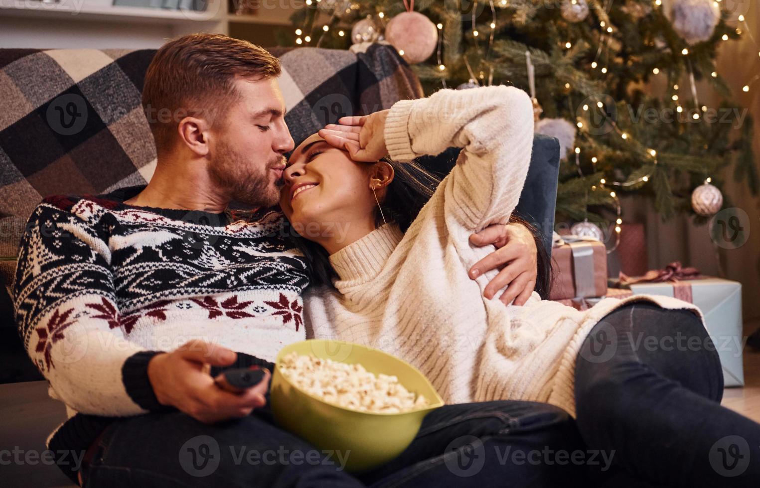 Young couple indoors in christmas decorated room sitting on the floor and celebrating new year photo