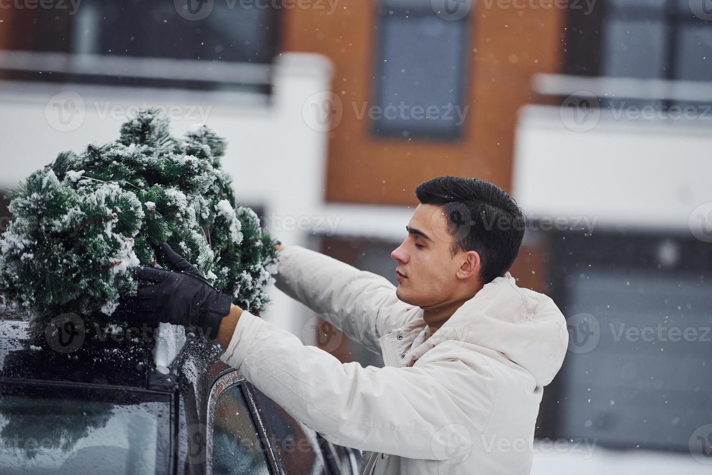 Man in white wear putting christmas fir tree on the top of his car