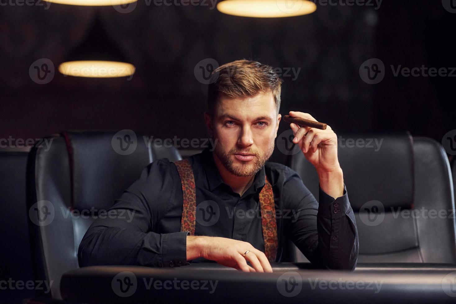 Elegant young man with cigarette sits in casino and plays poker game photo