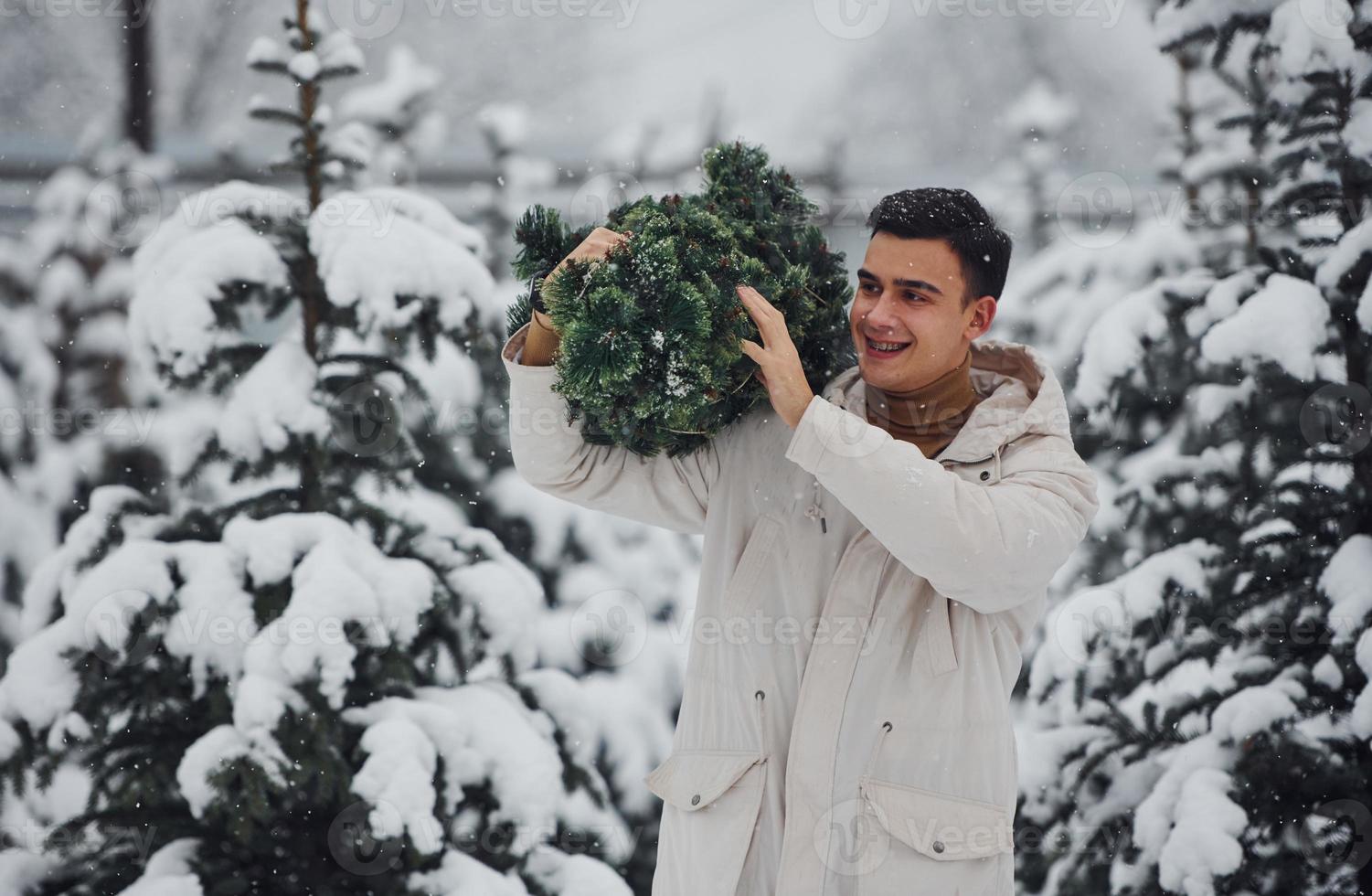 Young handsome man carrying fresh cutted fir tree outdoors photo