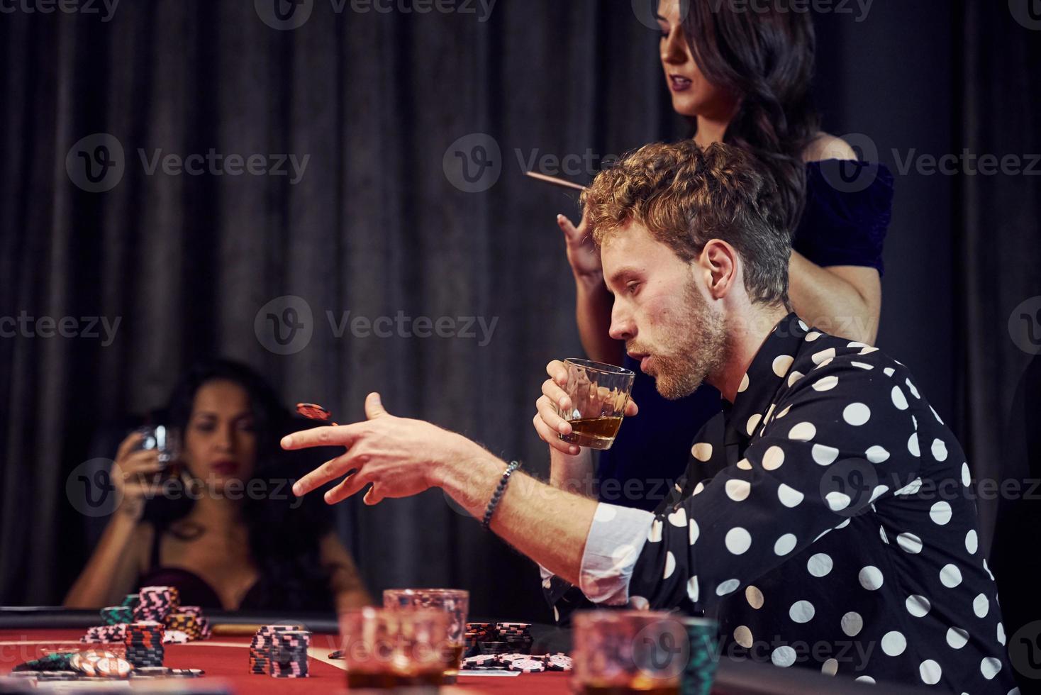 With glasses of drink. Group of elegant young people that playing poker in casino together photo