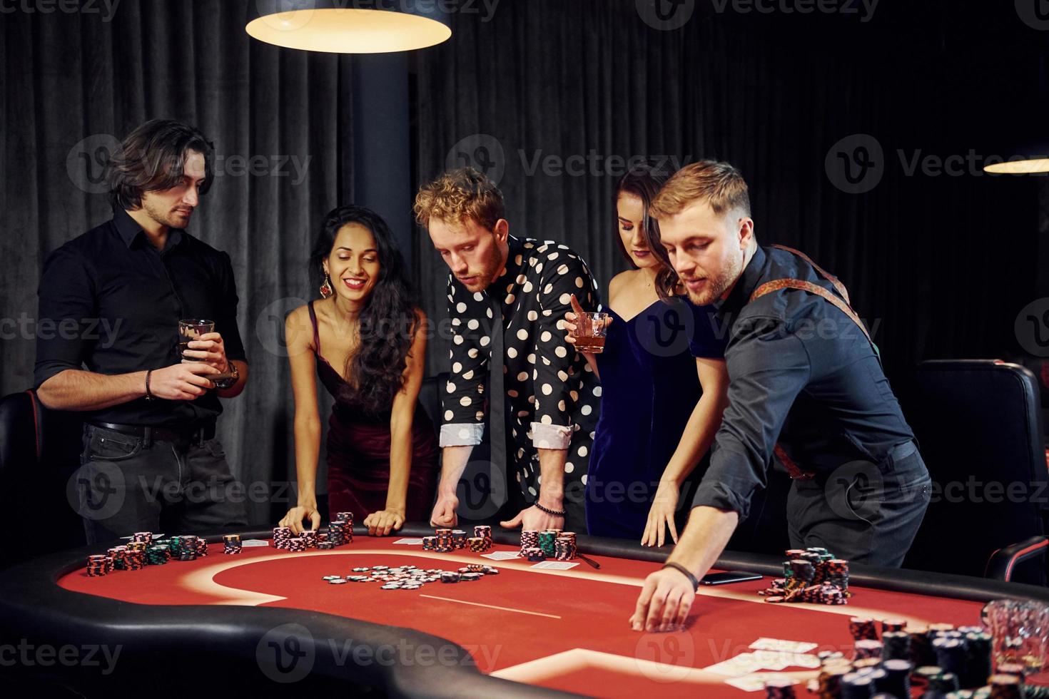 People in elegant clothes standing and playing poker in casino together photo