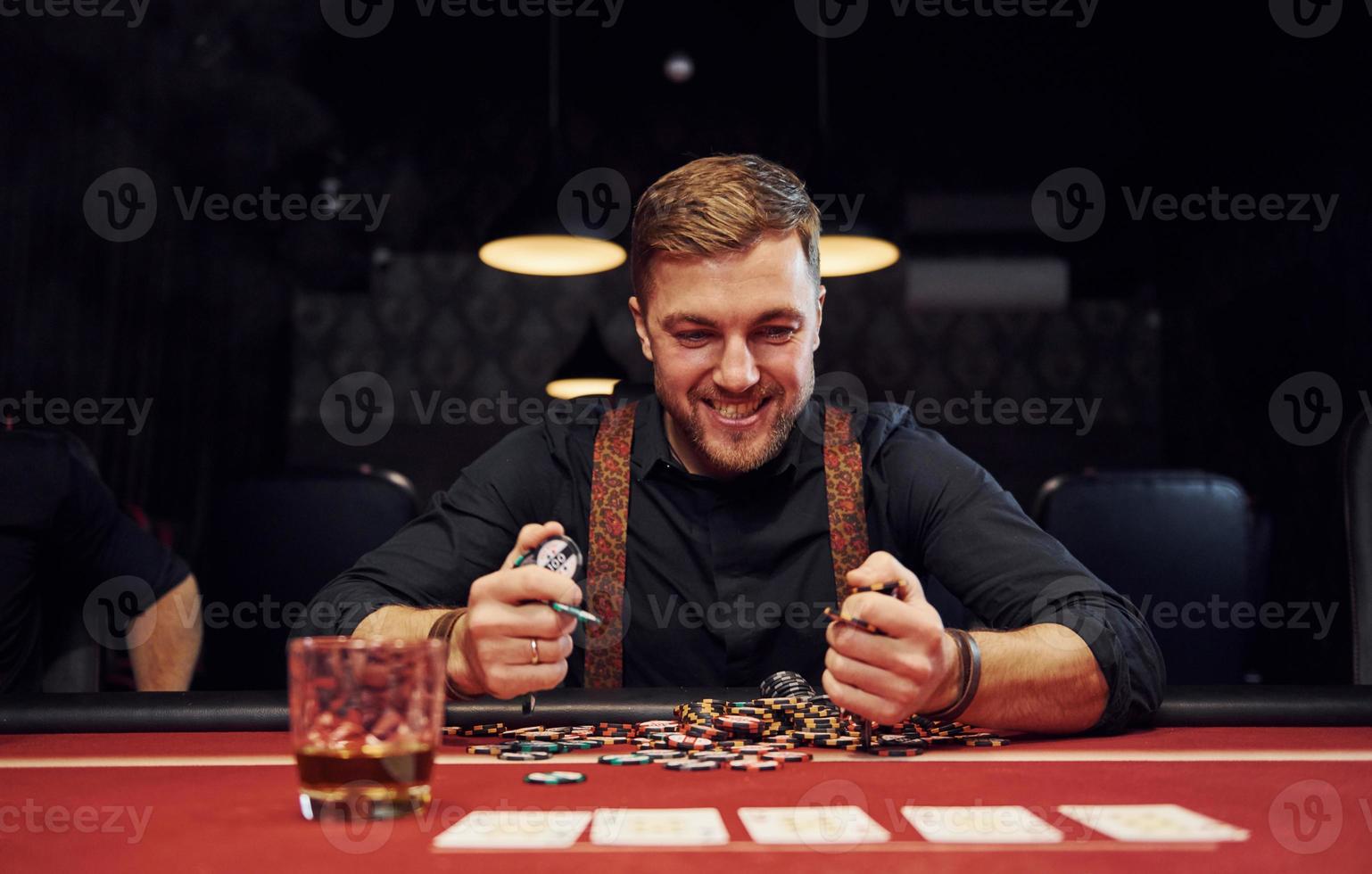 Happy elegant young man sits in casino and celebrate his victory in poker game photo