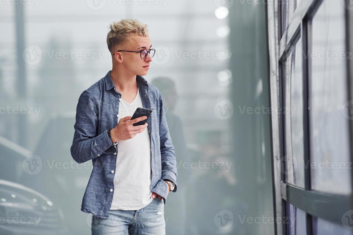 Young hipster guy in nice clothes stands indoors against grey background photo