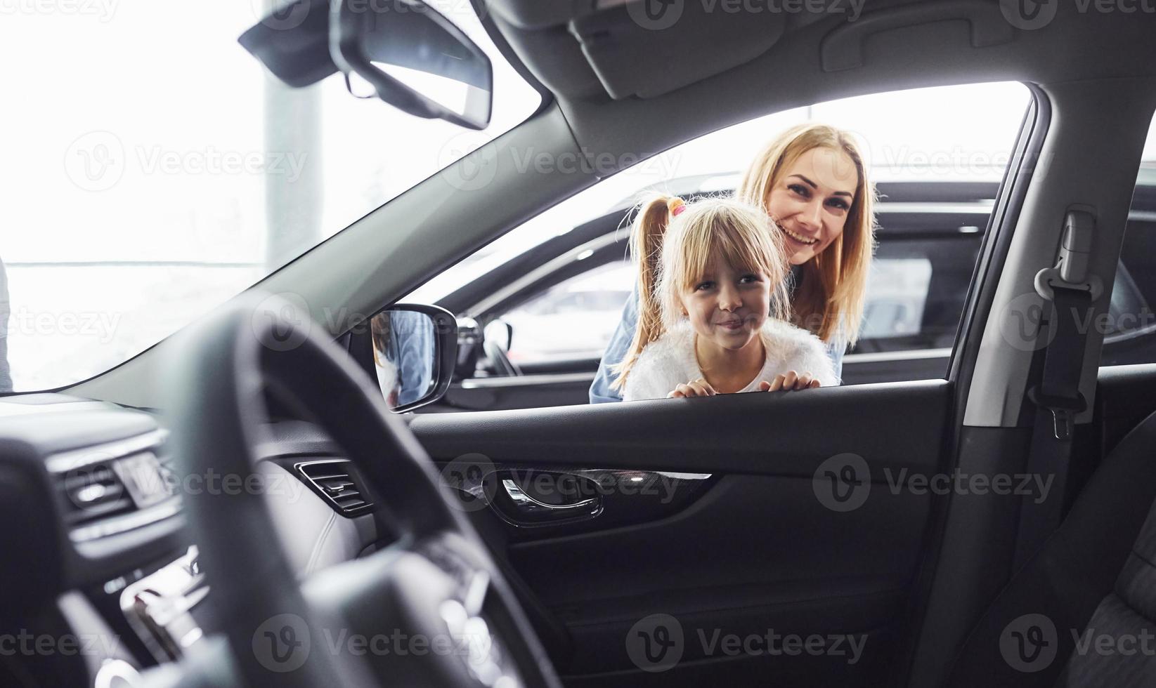 Mother and daughter looking inside modern new car in salon photo