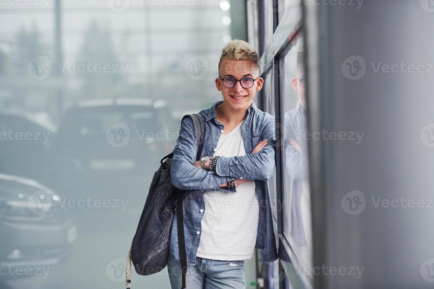 un joven hipster con ropa bonita se para en el interior contra un fondo gris foto