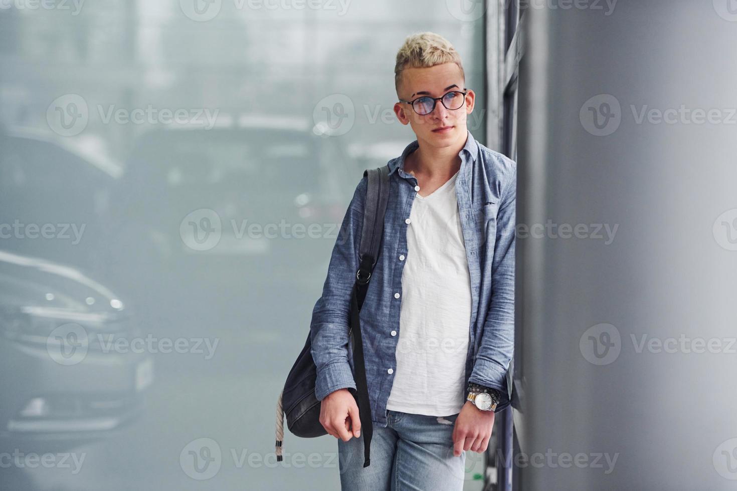Young hipster guy in nice clothes stands indoors against grey background photo