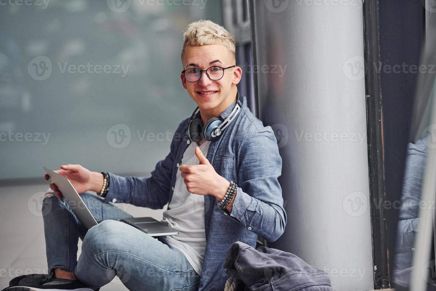 joven hipster con ropa bonita sentado en el interior cerca de un fondo gris foto