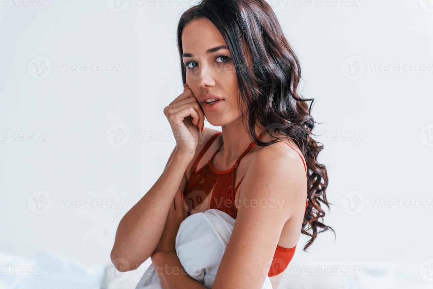 Portrait of beautiful young brunette that is in red underwear in white room photo