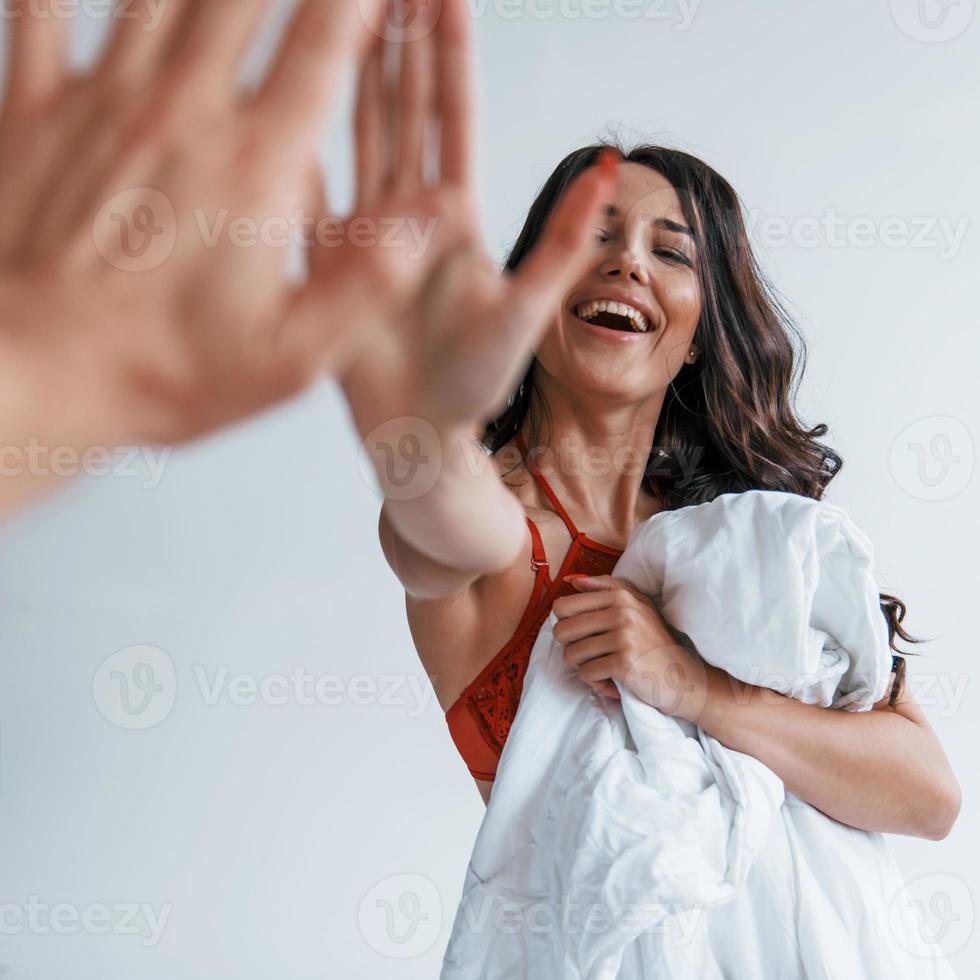 Positive beautiful young brunette in underwear in white room gives high five to the other person photo