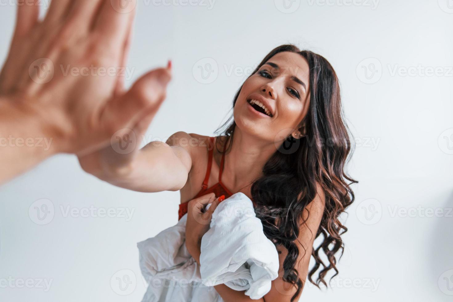 Positive beautiful young brunette in underwear in white room gives high five to the other person photo