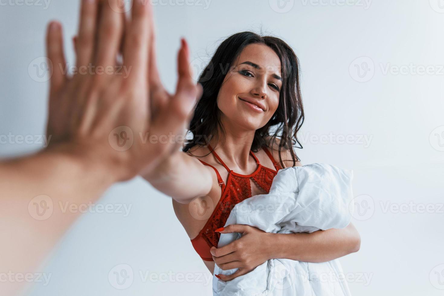 Positive beautiful young brunette in underwear in white room gives high five to the other person photo