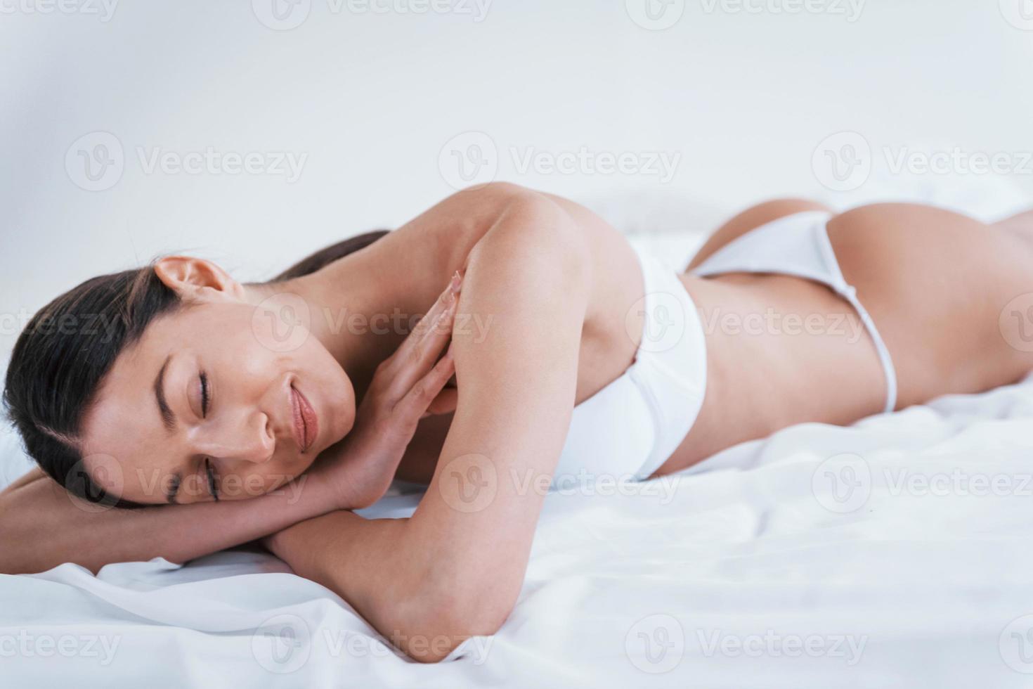Young woman in underwear and with nice body shape lying down in the studio against white background photo